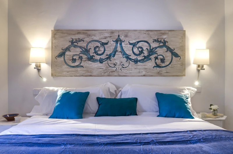 Ein gemachtes Bett mit blauen Kissen und handbemaltem Kopfteil